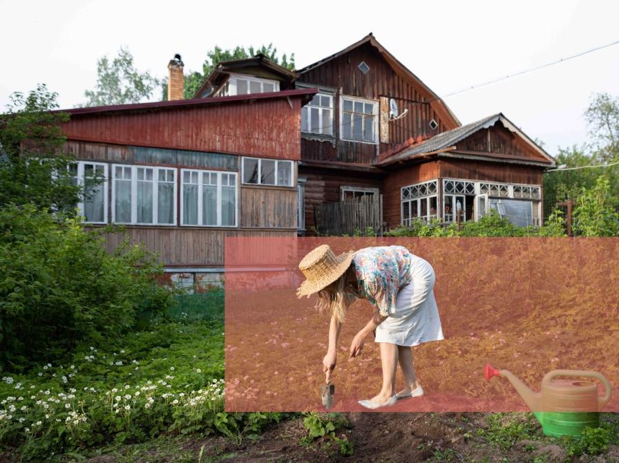 Kvinde graver i jorden med en skovl foran et gammelt hus